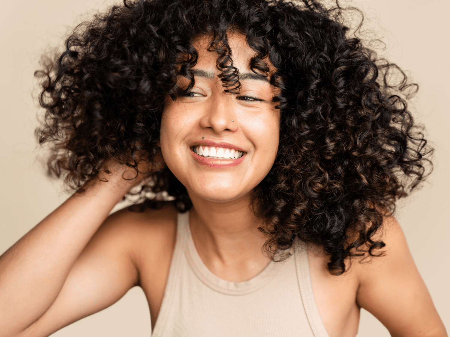 Close up of a woman with curly shot smiling and looking off to the side of the camera.