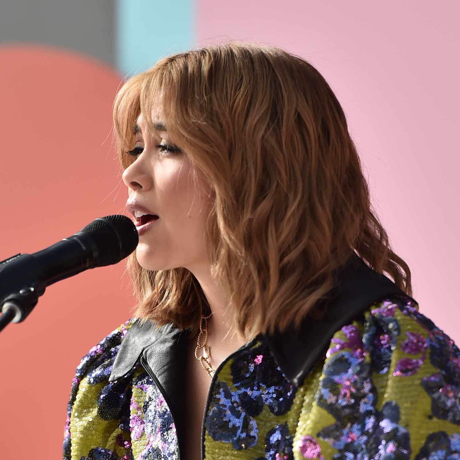 Hayley Kiyoko sings while wearing a shoulder-length hairstyle with bangs and messy face-framing layers