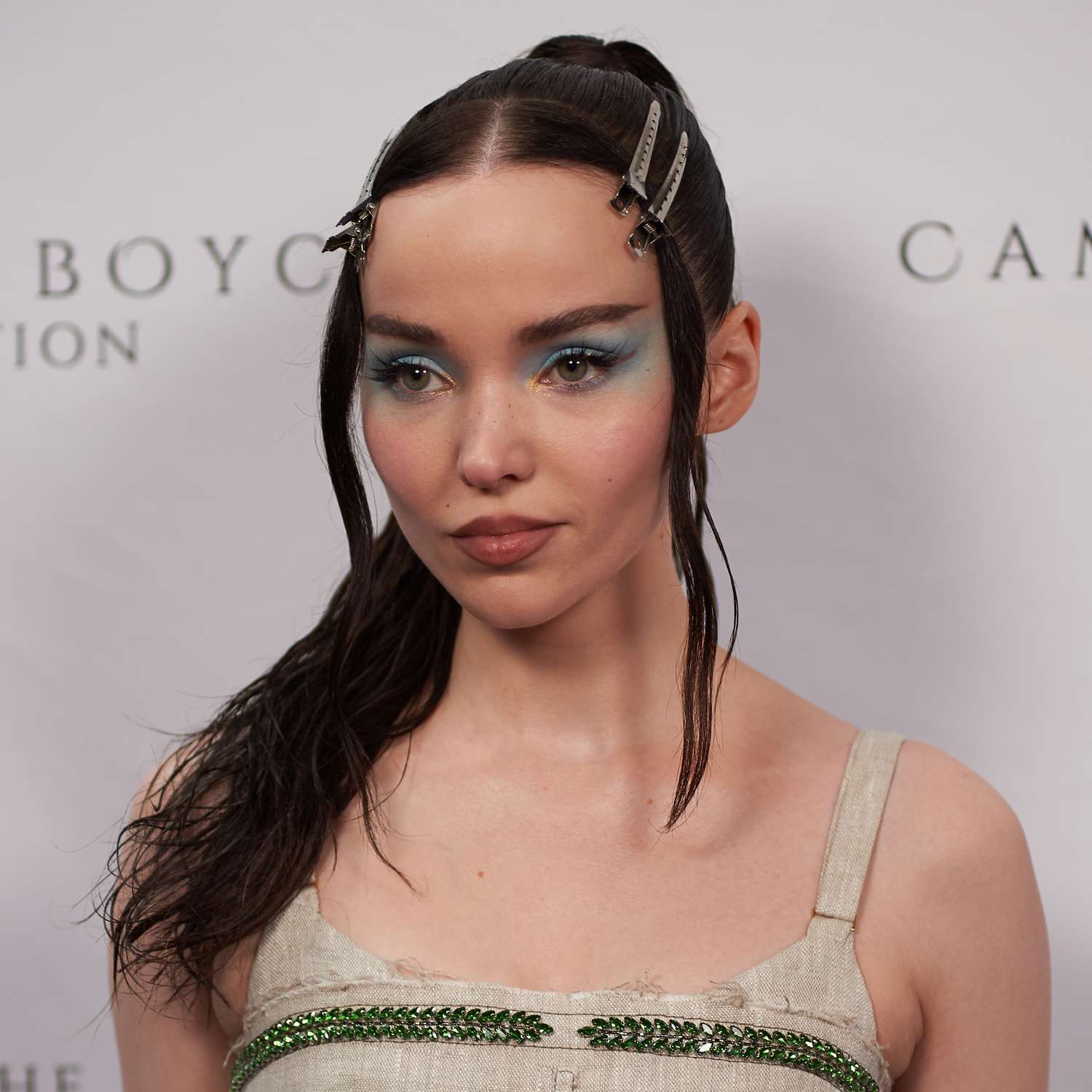 Dove Cameron wears a "wet" high ponytail and uses duck bill clips to pin back her front, face framing layer