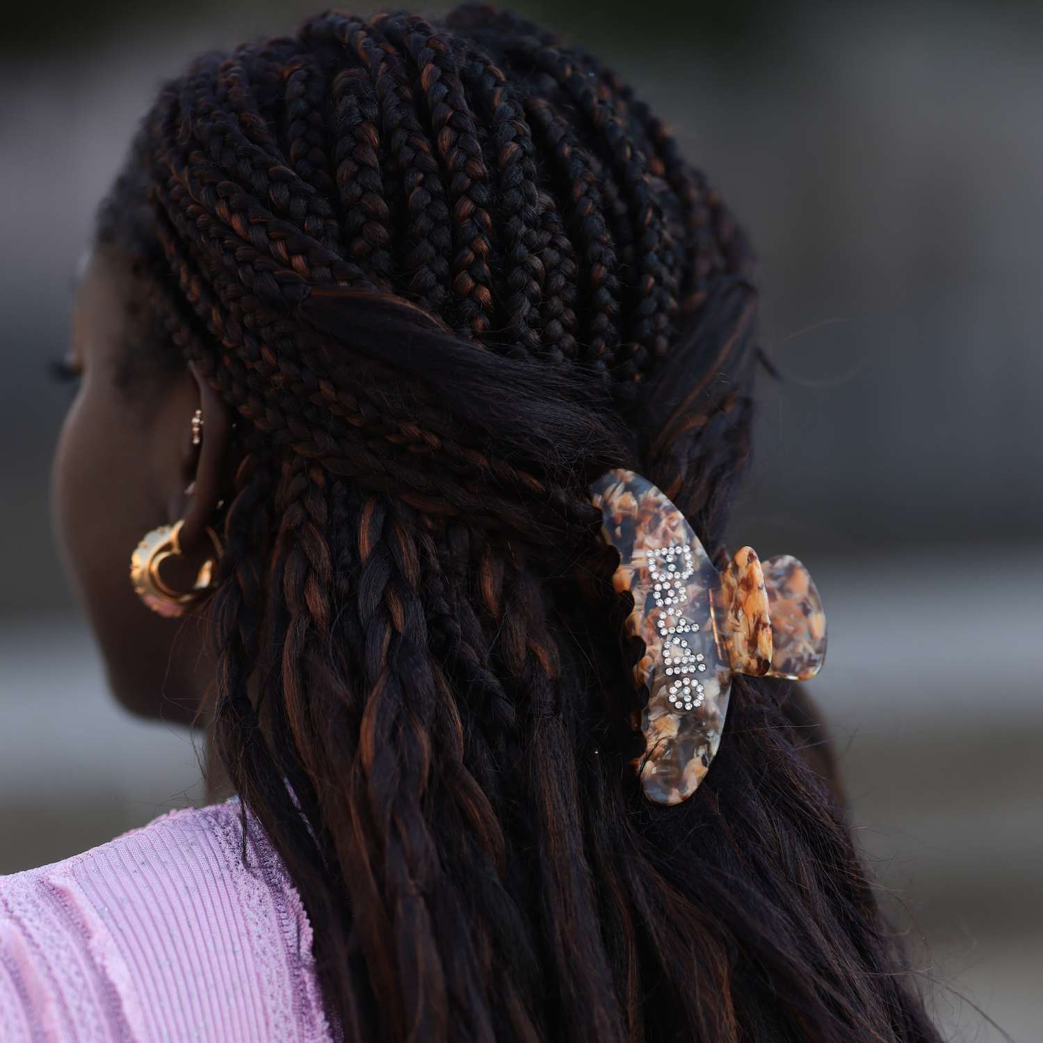 Lois Opoku wears her braids in a half up style using a a tortoise colored claw clip with rhinestone text