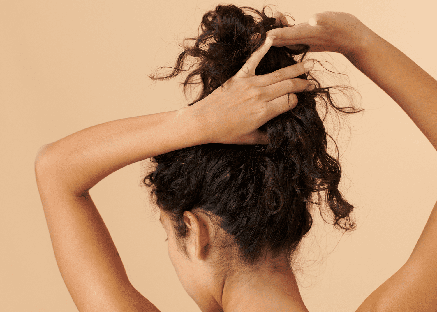 Woman lifting her long brown curly hair with her hands