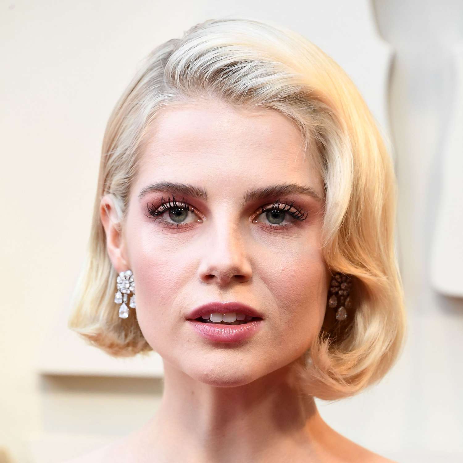 Lucy Boynton wears a strong wavy shape around the hairline of her platinum bob at the Oscars